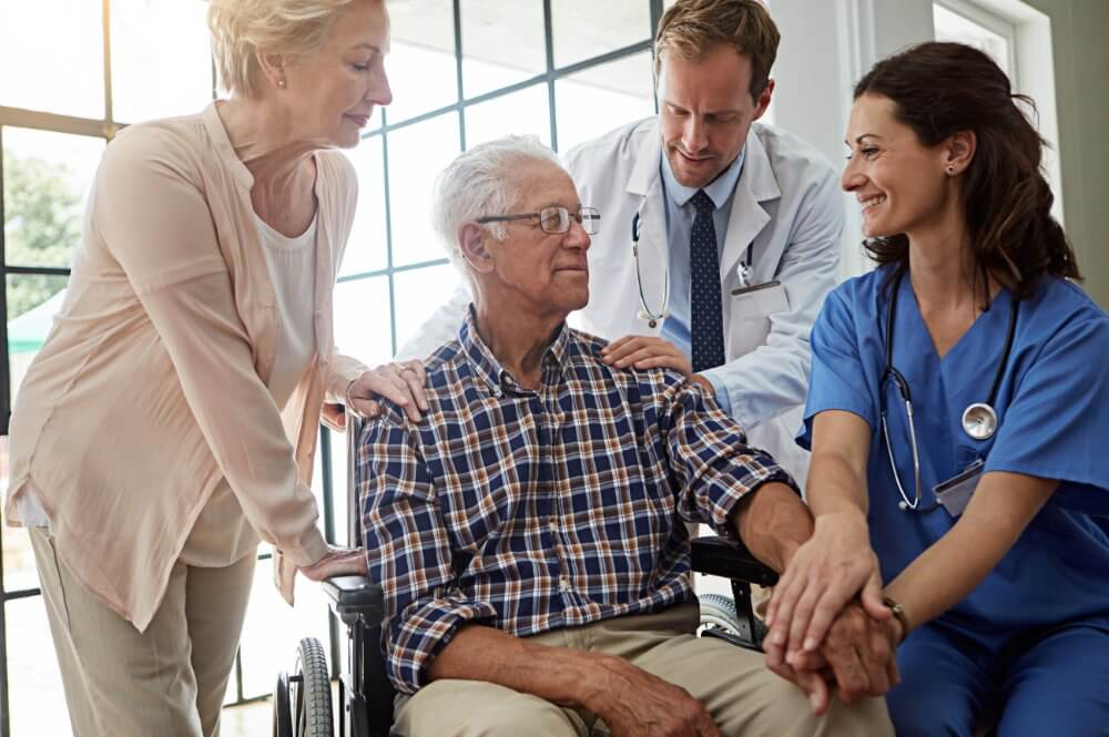 A group of doctors and nurses surround an elderly man in a wheelchair, demonstrating patient support systems in action.