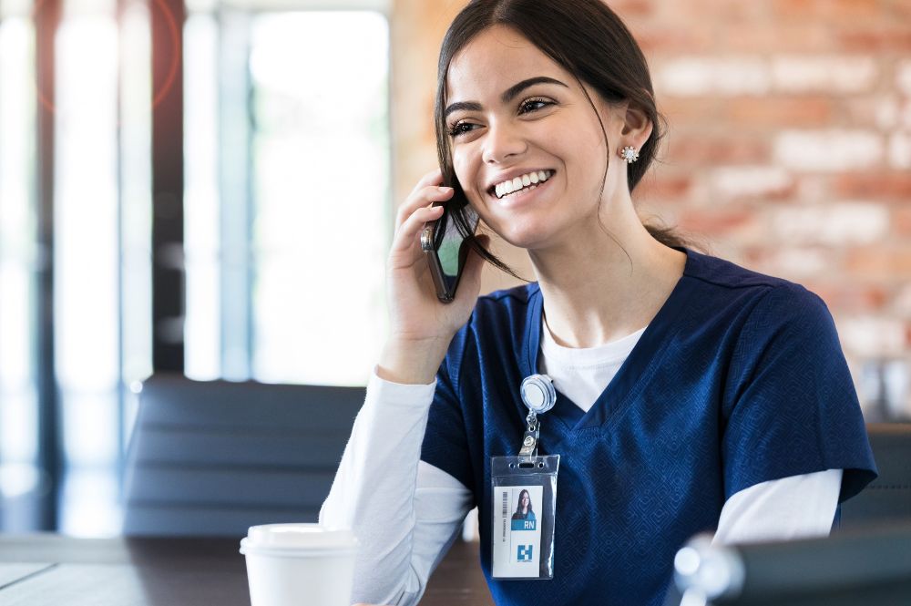 A woman in scrubs talking on the phone, discussing PSP technology integration in a healthcare setting.