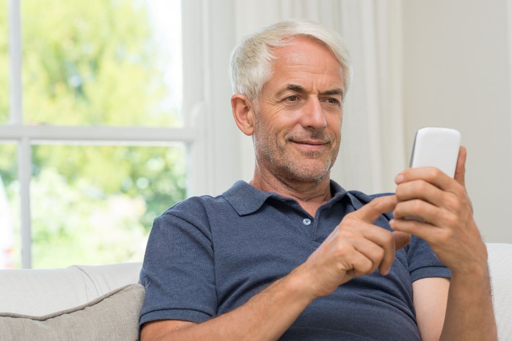 An older gentleman on his cell phone following the medication adherence given to him by his doctor.