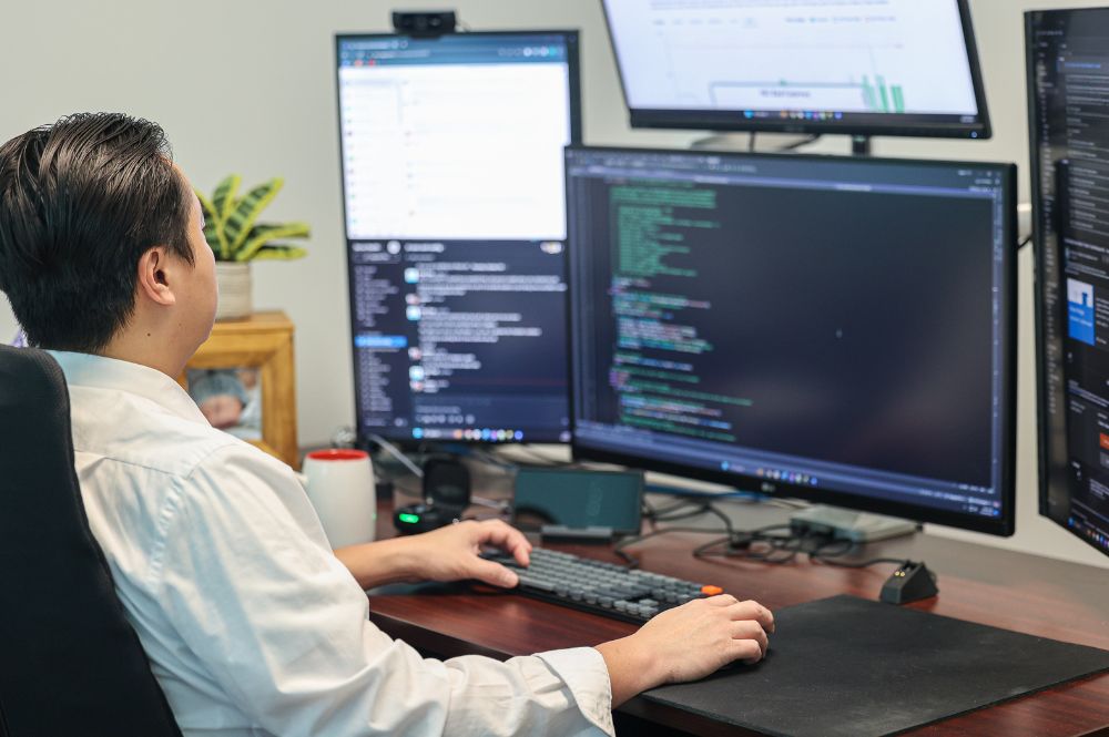 Professional software developer using multiple monitors to build no-code platforms for patient support programs
