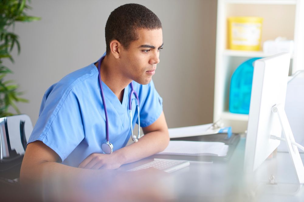 Male doctor in scrubs sitting at a desk, reviewing PSP deployment best practices for patient care improvements.
