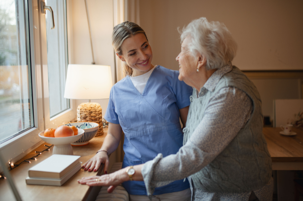 Nurse and elderly woman discuss rare disease PSP challenges by a window, highlighting the importance of support and care.