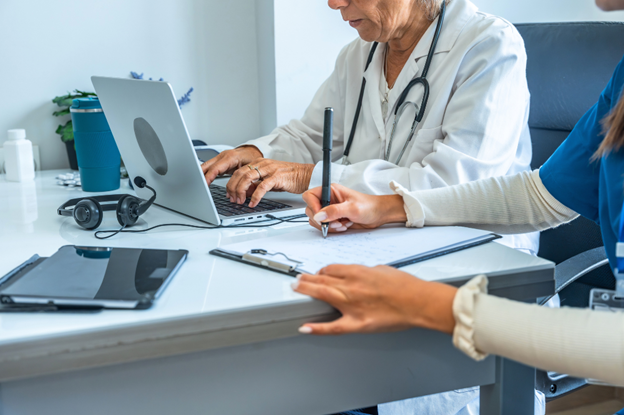 A doctor assista a nurse in reviewing medical records on a laptop