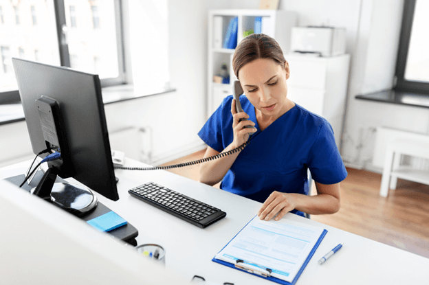 A healthcare professional in scrubs speaks on the phone at her desk, highlighting patient support programs and access to care.